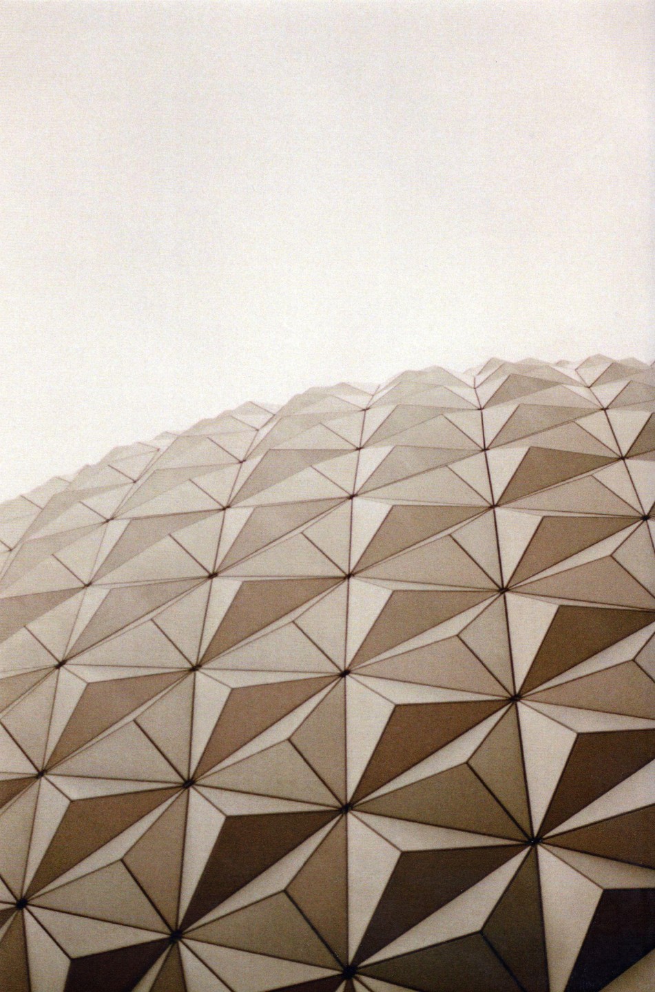 A geodesic dome with triangular panels is photographed from a low angle against a bright sky.