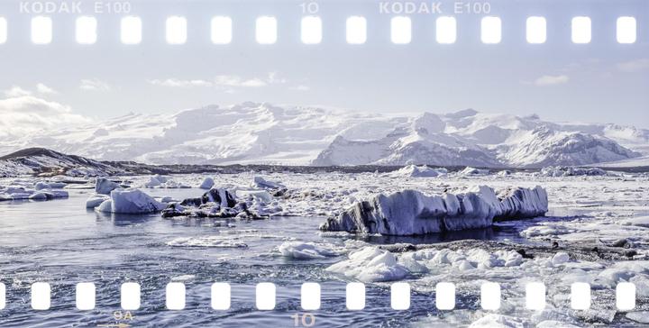 Icebergs float in a body of water with snow-covered mountains in the background.