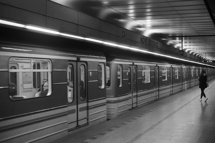 A woman walks along a subway platform next to a train with a man visible through a window.