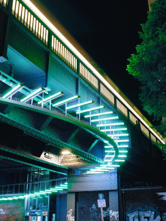 A bridge with neon lights and a tree is visible at night.