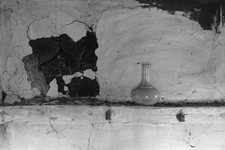 A glass bottle sits on a ledge against a cracked and peeling wall.