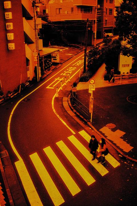 Two people walk across a crosswalk on a street in a city.