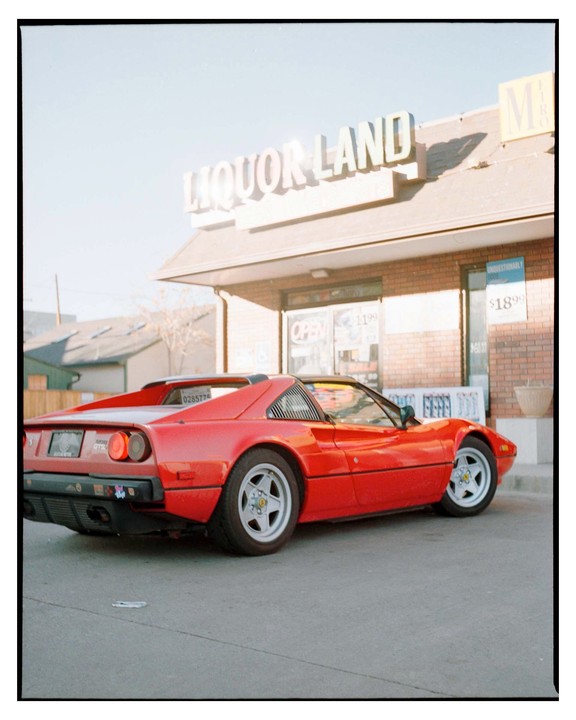 A red Ferrari 308 GTS is parked in front of a Liquor Land store.
