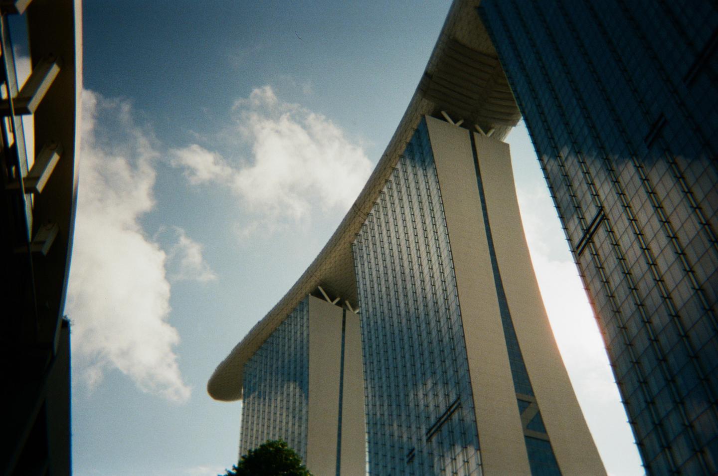 Three modern skyscrapers with a curved roof are visible from a low angle against a cloudy sky.