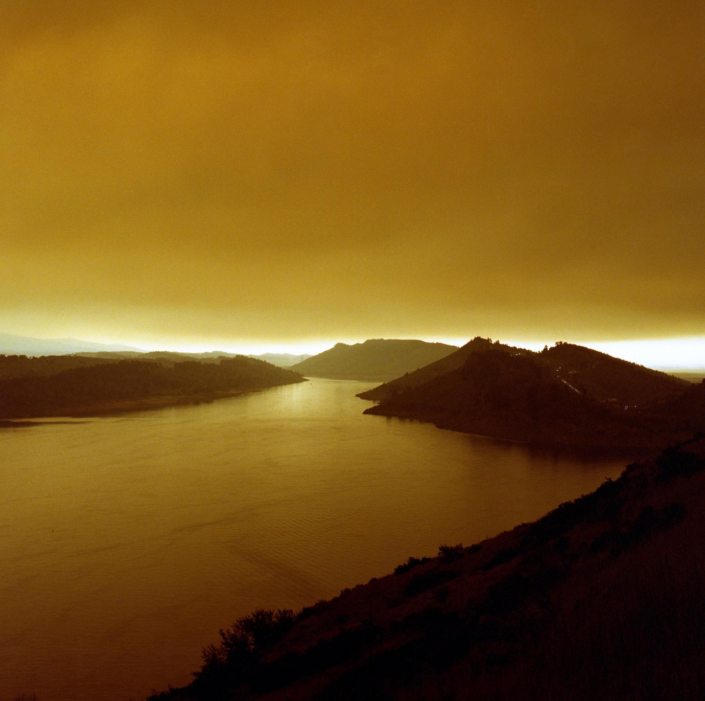 A body of water flows between hills under a hazy, golden sky.