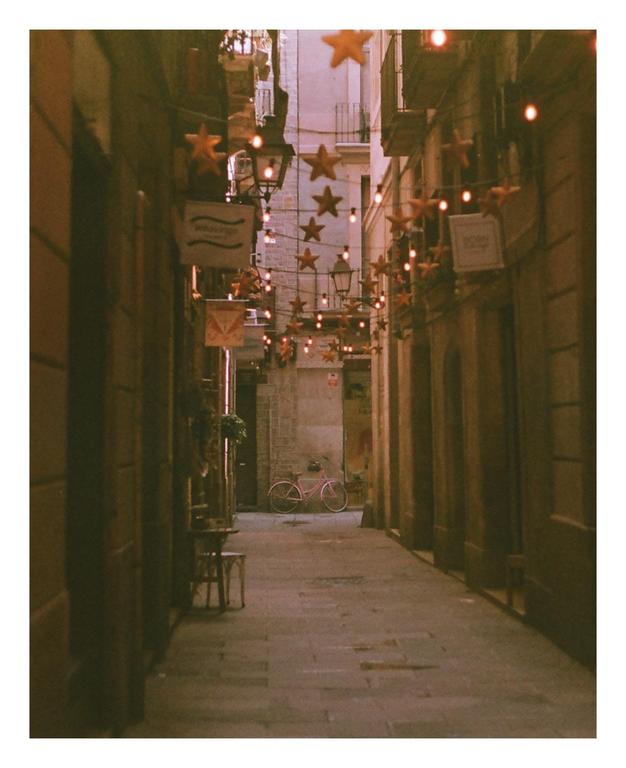 A narrow street in Barcelona is decorated with star-shaped lights strung between buildings.