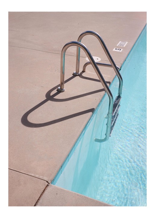A metal ladder descends into the clear blue water of a swimming pool, casting a shadow on the concrete edge.