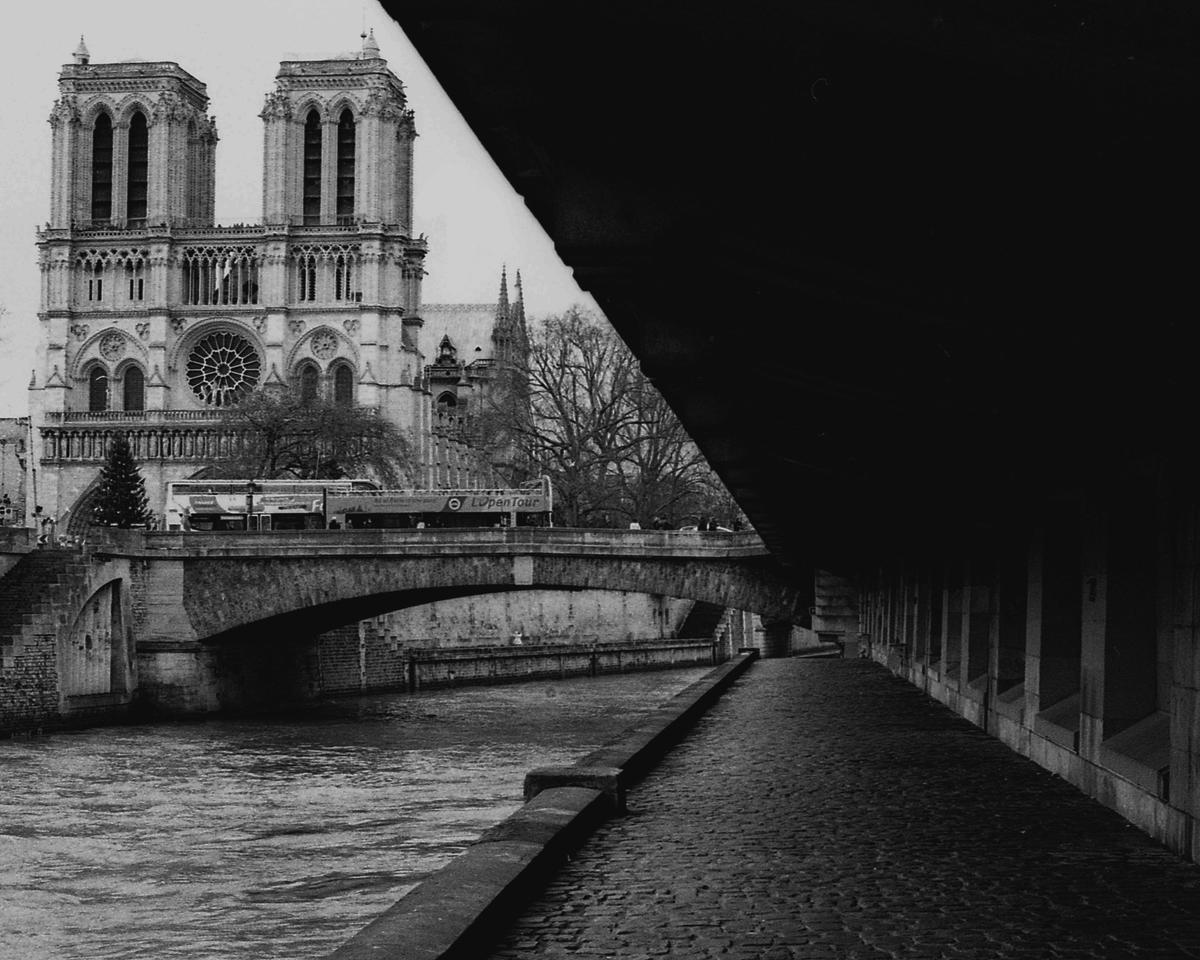 Notre Dame Cathedral is visible across a river and bridge, with a dark underpass in the foreground.