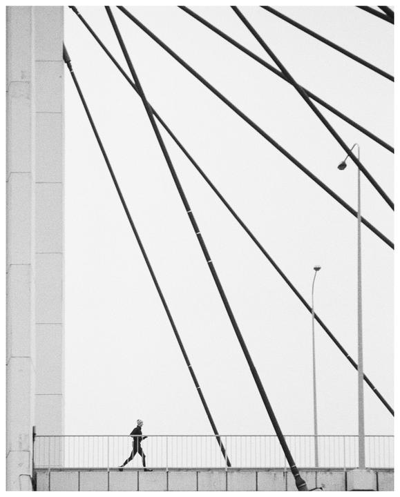 A person walks along a bridge with diagonal cables and a street light.