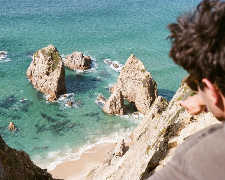 A person points to a beach with rock formations in the ocean.