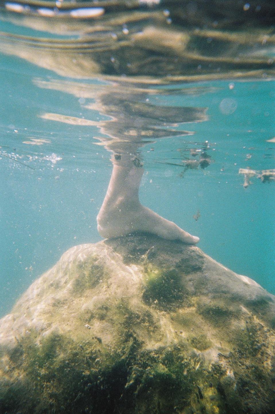 A foot rests on a rock underwater with the surface of the water visible above.