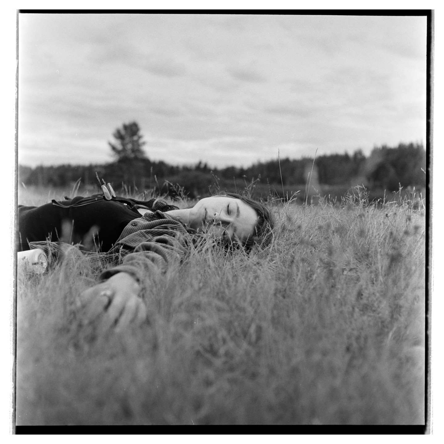 A woman lies in a field of tall grass with her eyes closed.