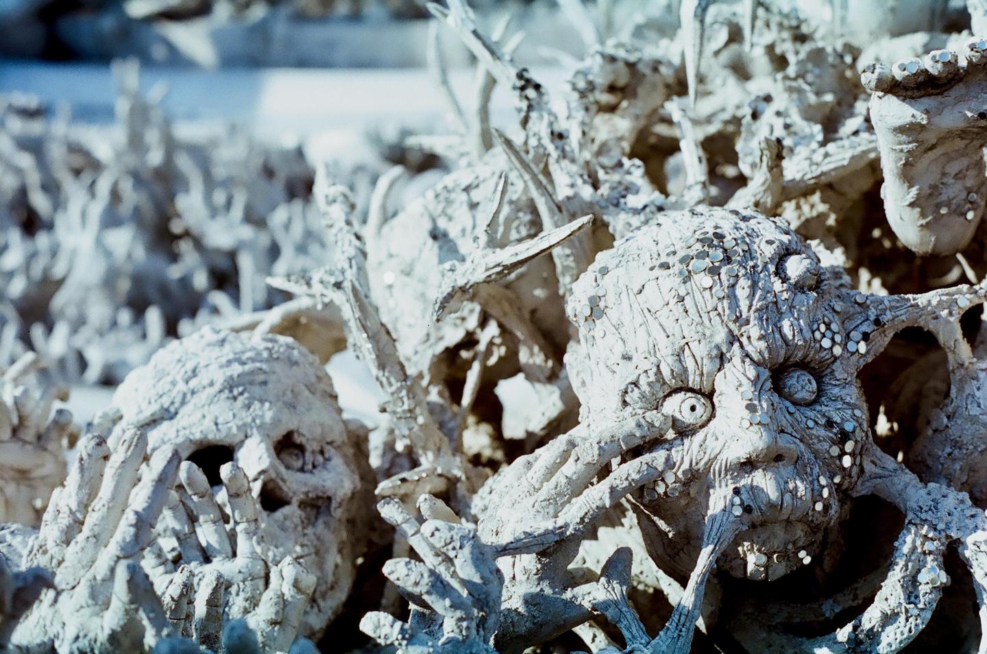 Two white, skeletal, demonic faces with coins embedded in them are visible in a close-up shot.