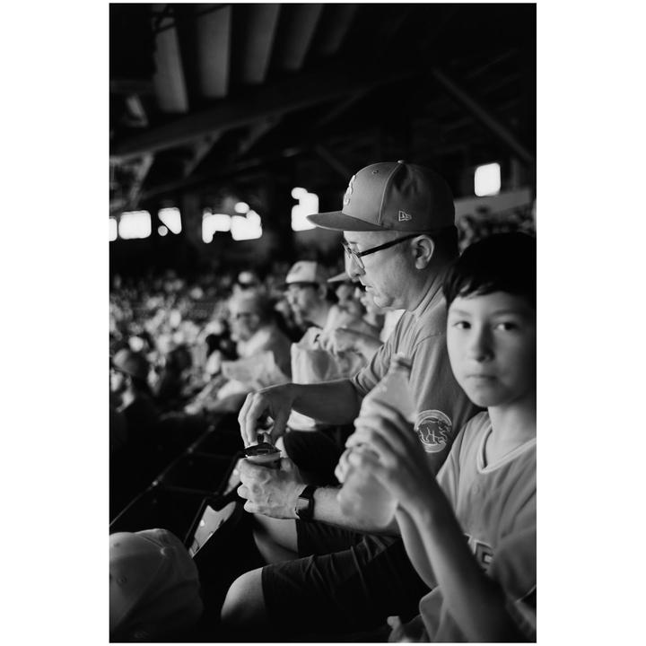 A man and a boy are sitting in a stadium with other spectators in the background.