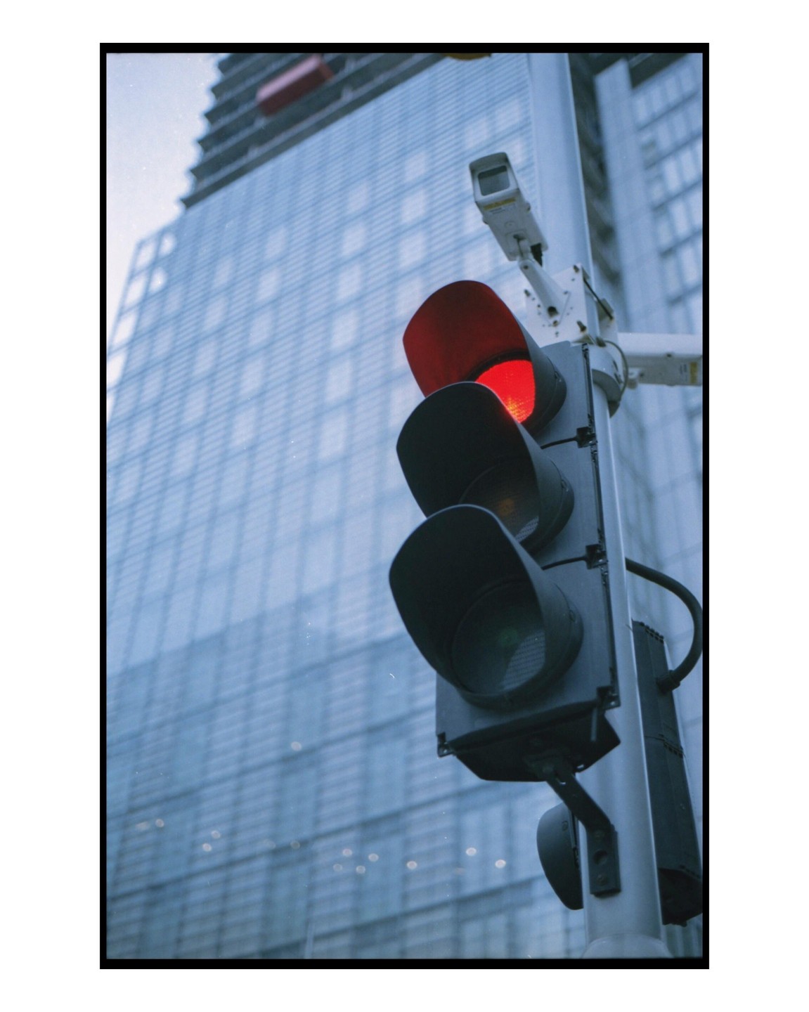 A traffic light with a red signal is mounted on a pole in front of a modern building with many windows.