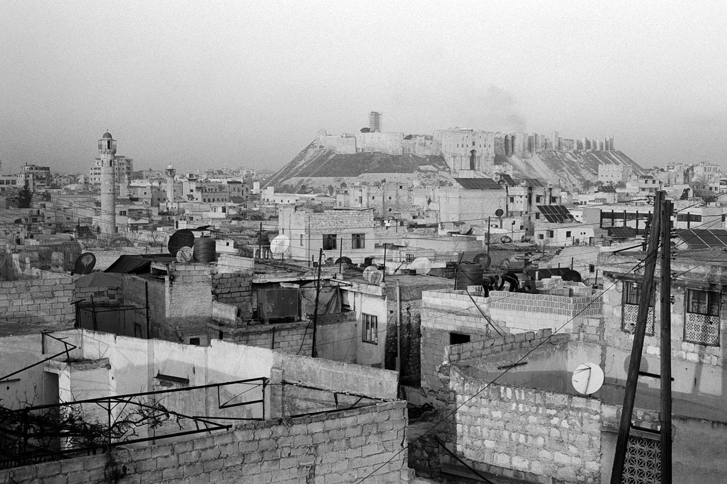 A black and white cityscape shows a dense collection of buildings with a large citadel on a hill in the background.