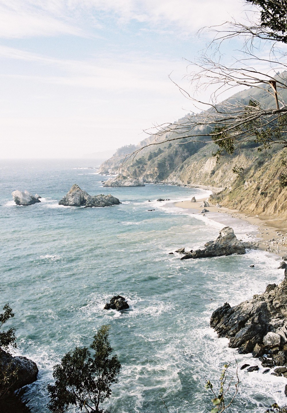 A rugged coastline with a sandy beach and rocky outcrops is visible from a high vantage point.