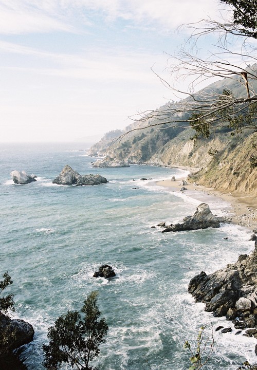 A rugged coastline with a sandy beach and rocky outcrops is visible from a high vantage point.