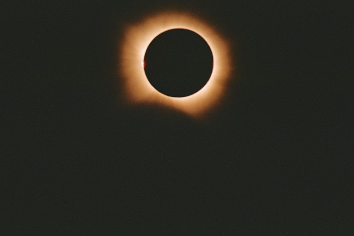 The sun is visible during a total solar eclipse, with a bright corona around the dark disk of the moon.