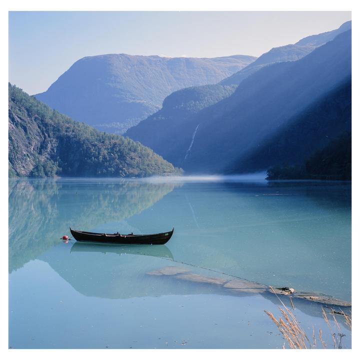 A small boat floats on a misty lake surrounded by mountains with a waterfall.