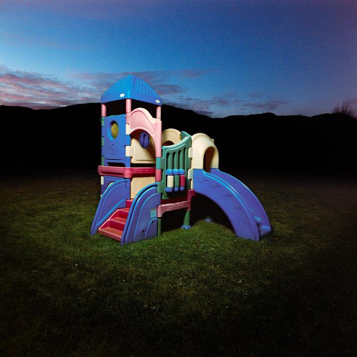 A colorful plastic playground structure sits on a grassy lawn under a twilight sky with a dark mountain range in the background.