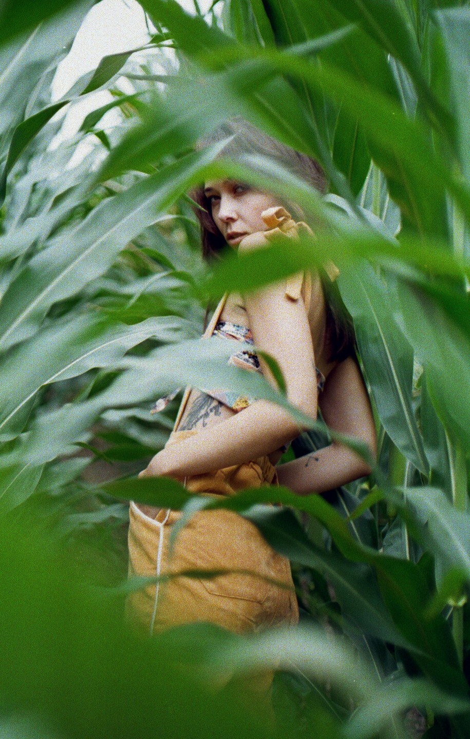 A woman with long hair and a yellow top is partially visible through tall green leaves.