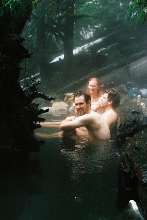 Three men are soaking in a natural hot spring surrounded by a lush forest.