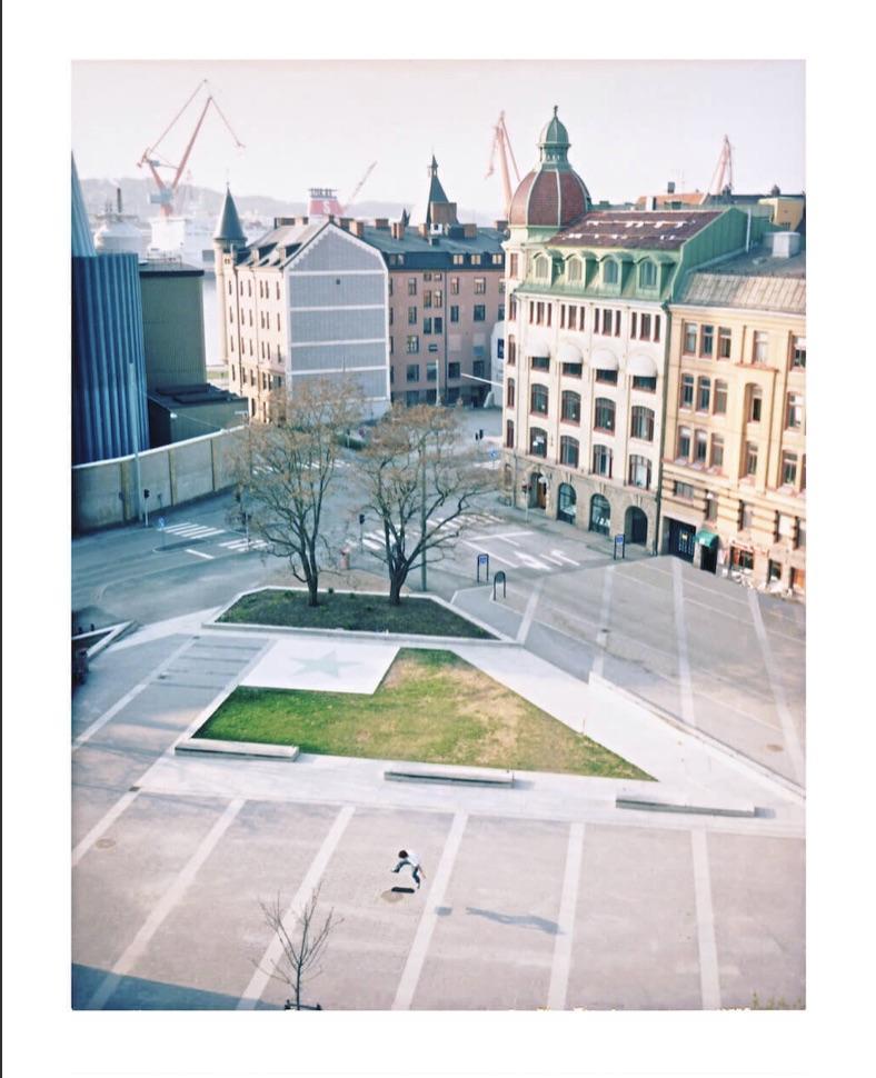 A high-angle view shows a city square with buildings and cranes in the background.