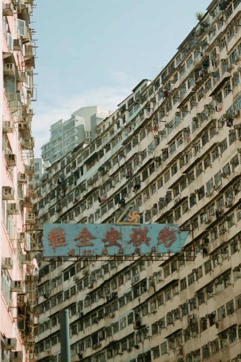 A blue sign with red lettering is visible between two tall, densely packed buildings.