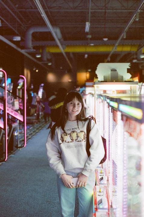 A woman stands in an arcade with bright neon lights and games surrounding her.