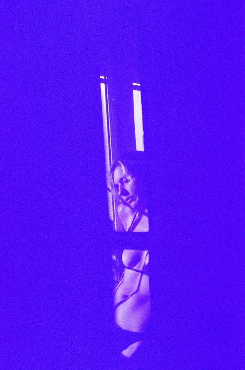 A woman is visible through a window with purple light and shadows.