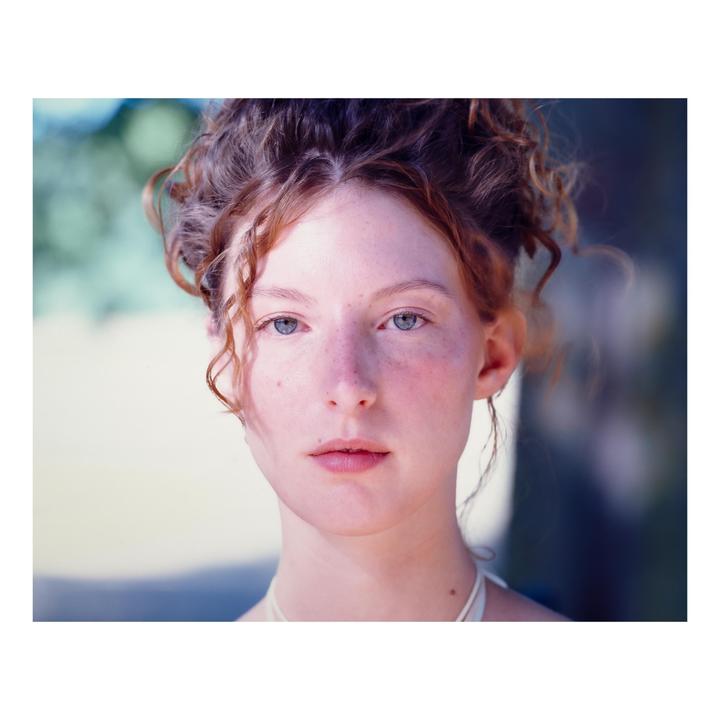 A woman with red curly hair and freckles looks directly at the viewer.