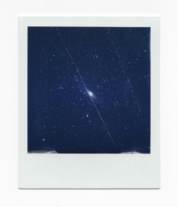 The Andromeda galaxy is visible in the night sky with many stars and light trails.
