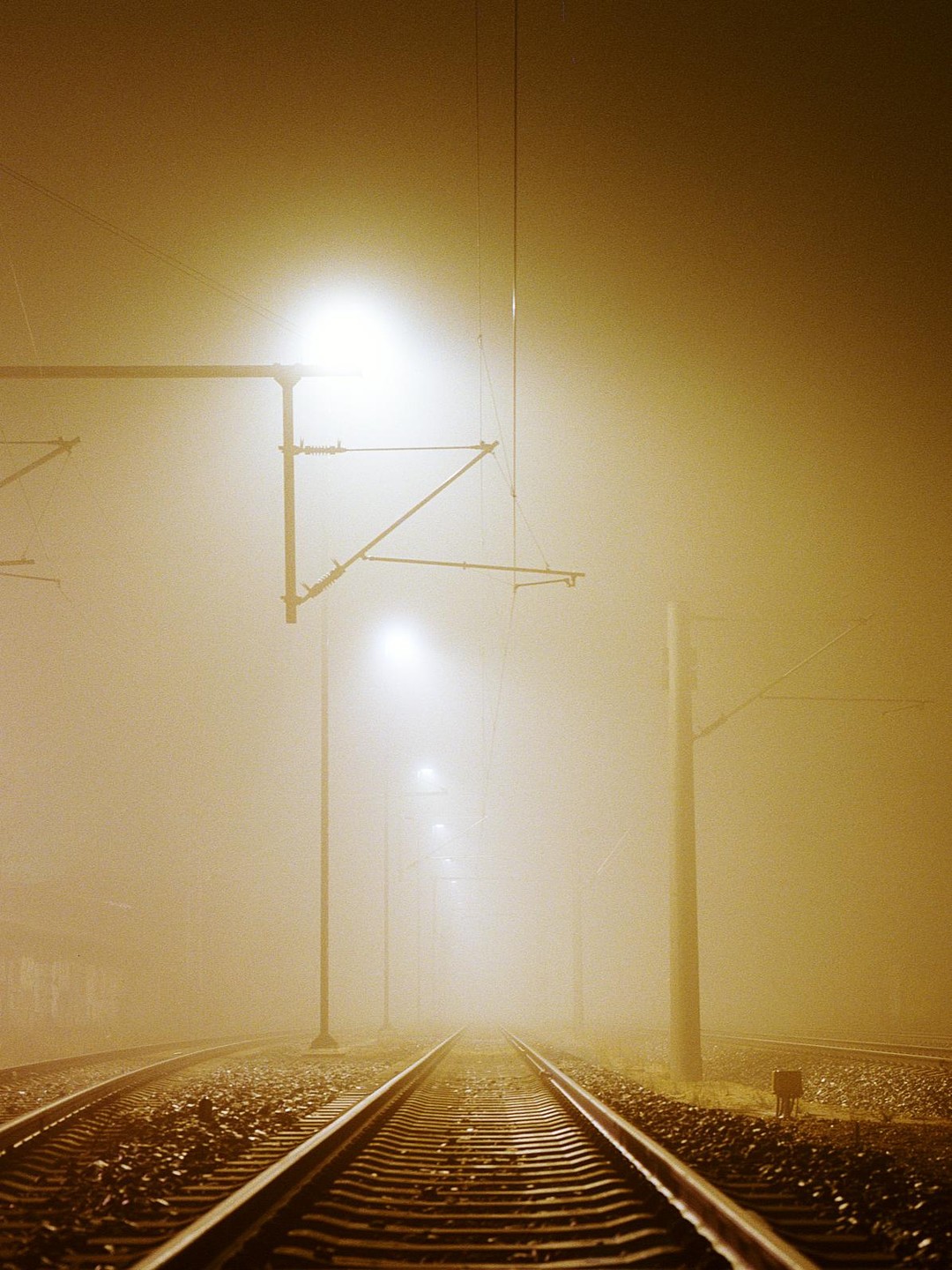 A long train track extends into the distance, illuminated by streetlights in a thick fog.
