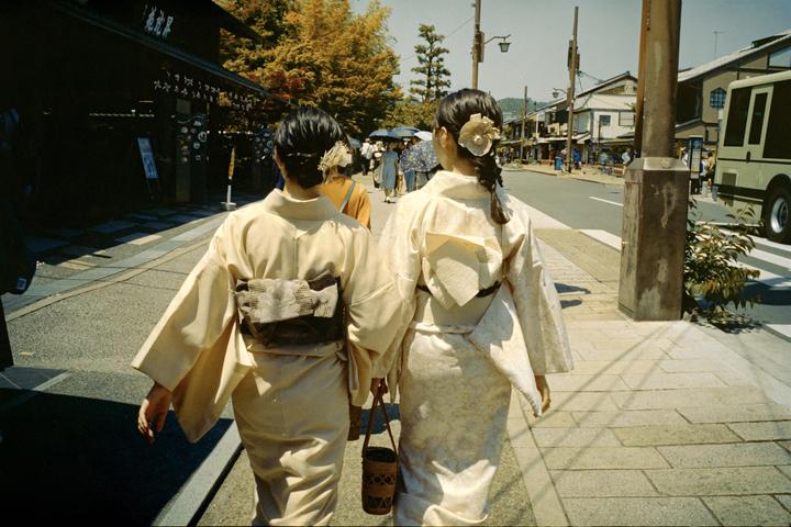 Two women in kimonos walk away from the viewer on a street in Kyoto.