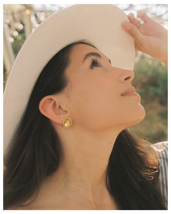 A woman wearing a wide-brimmed hat looks up, with her hand touching the brim.