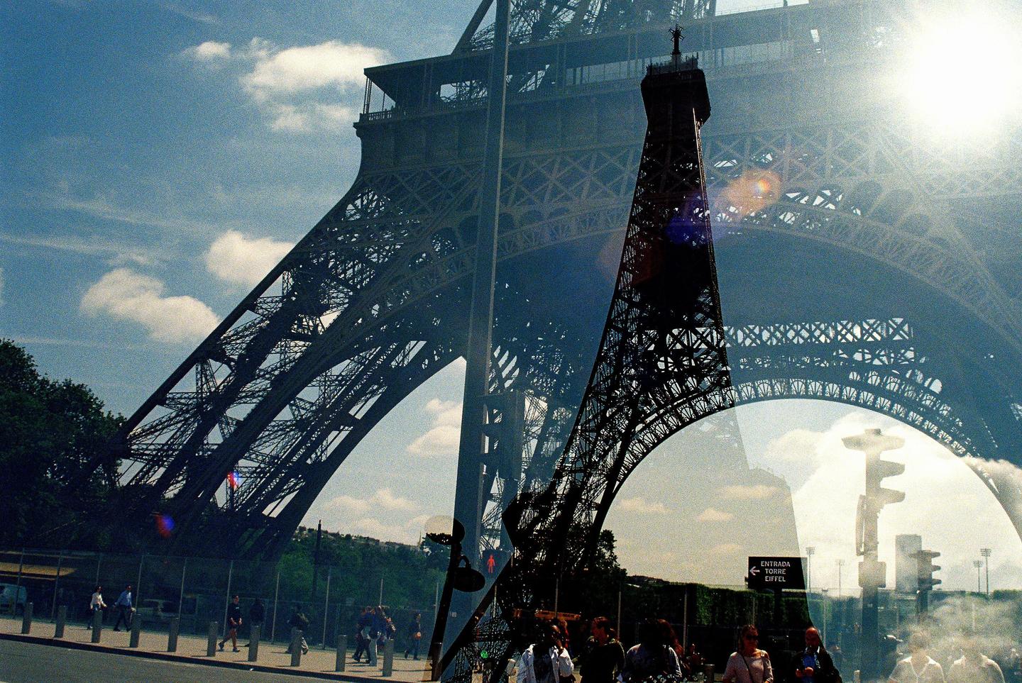 A double exposure shows the Eiffel Tower from two different perspectives, with people walking on the street below.
