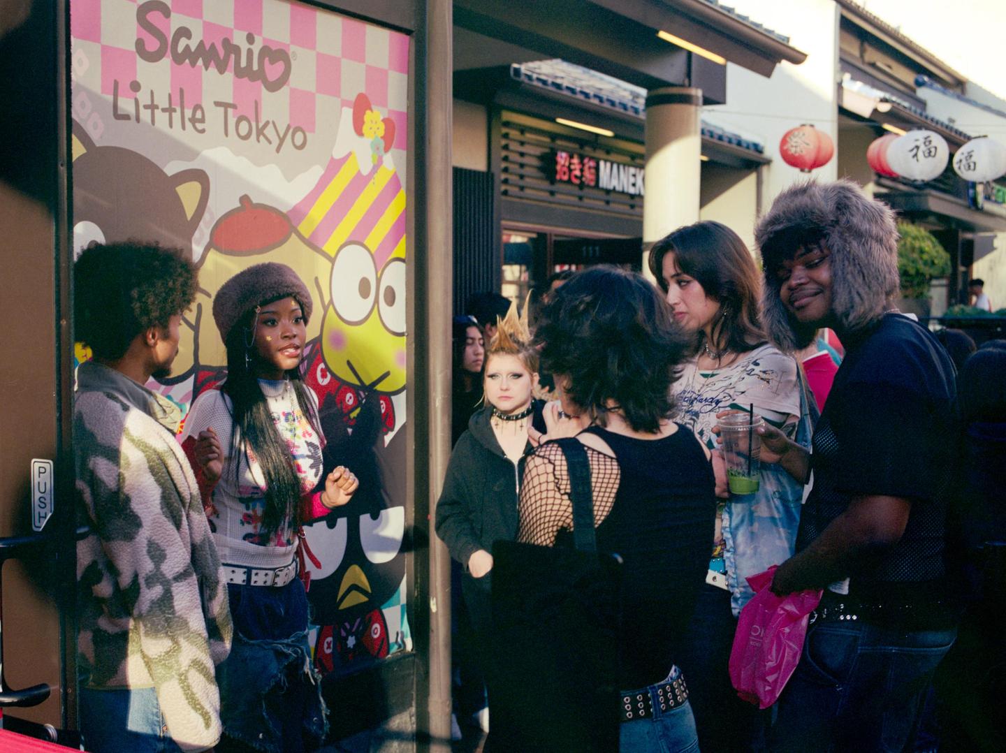 A group of young people are gathered on a street next to a colorful Sanrio Little Tokyo sign.