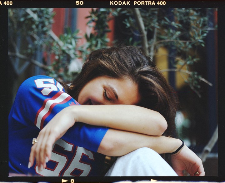 A woman with her eyes closed and head resting on her arm is wearing a blue jersey with white and red numbers.
