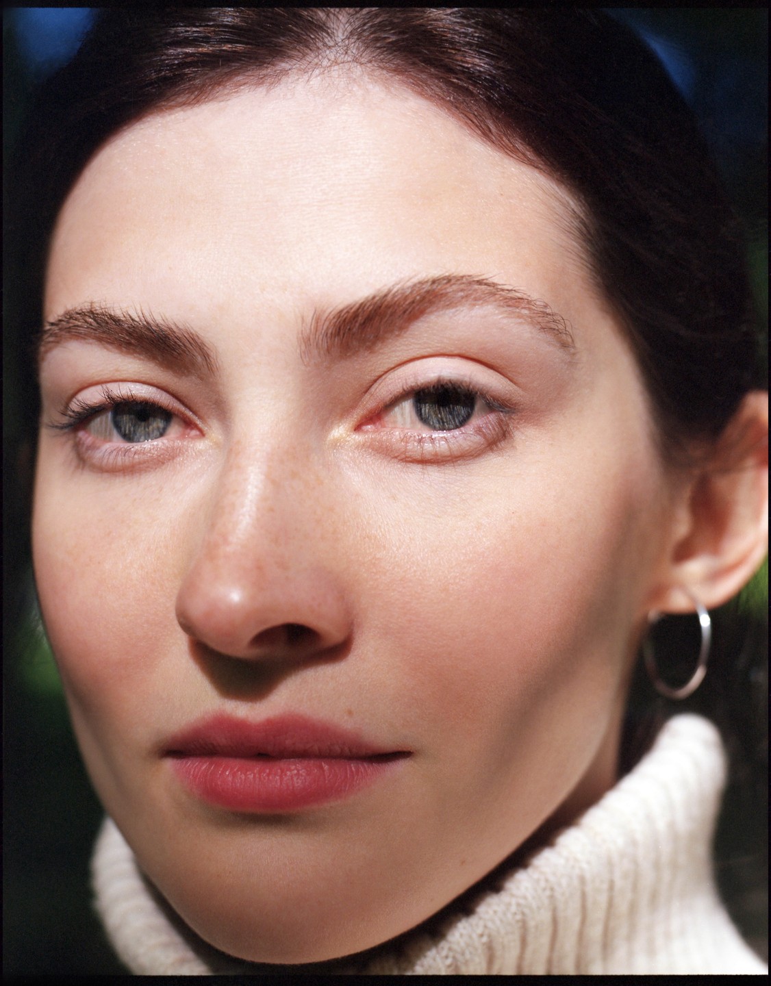 A woman with light skin and dark hair looks directly at the viewer.