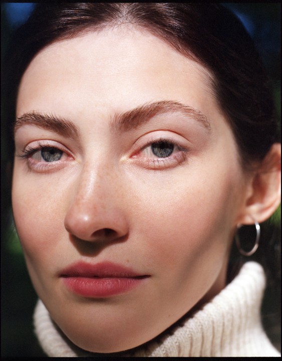 A woman with light skin and dark hair looks directly at the viewer.