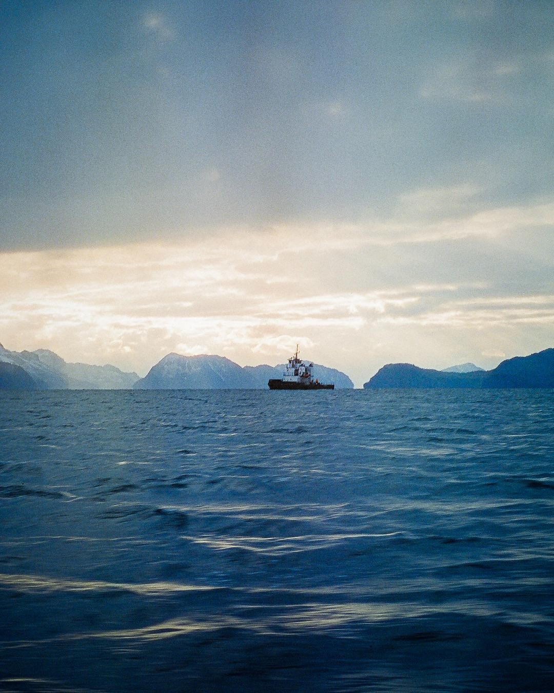 A boat floats on the water with mountains in the background under a cloudy sky.