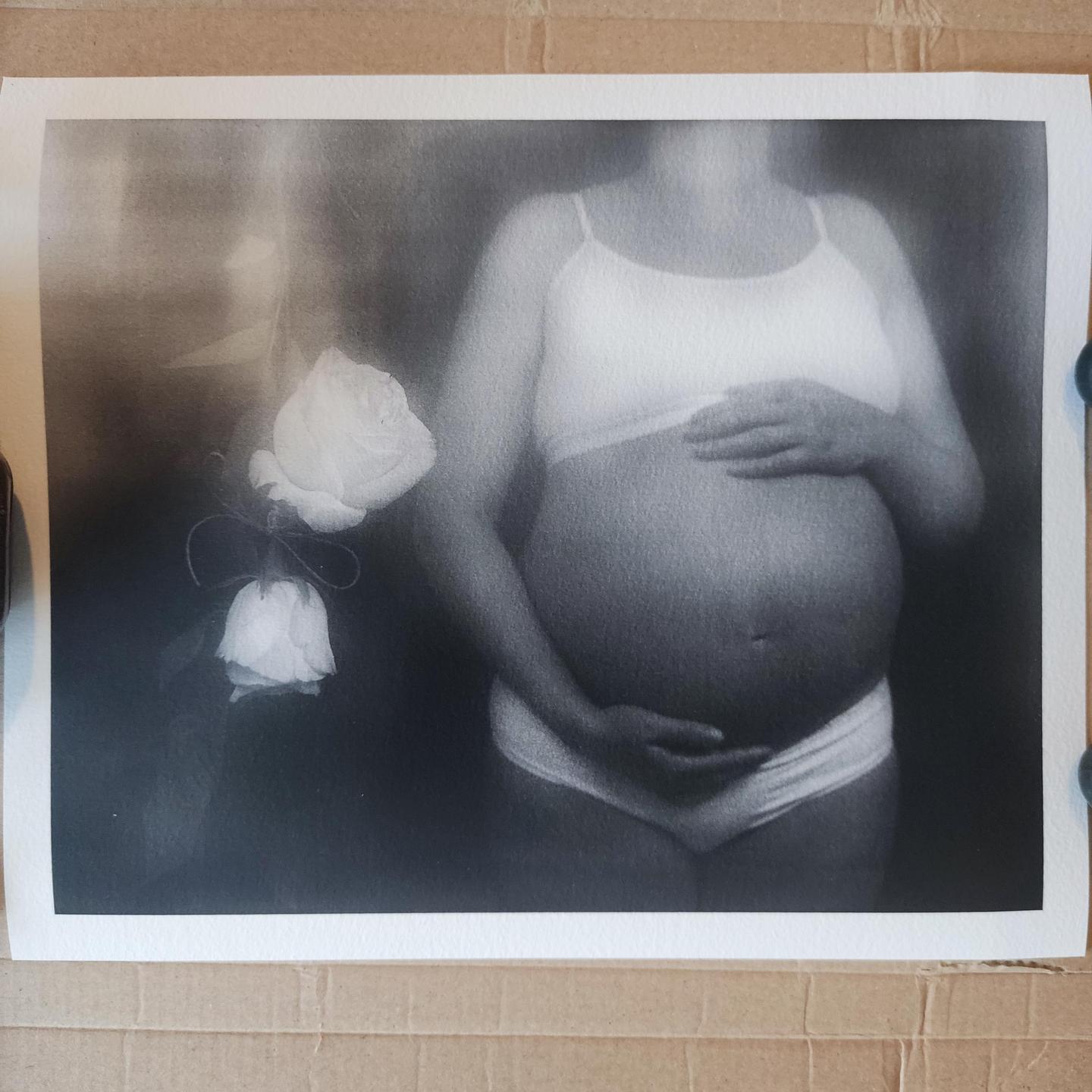A pregnant woman holds her belly while standing next to two roses.