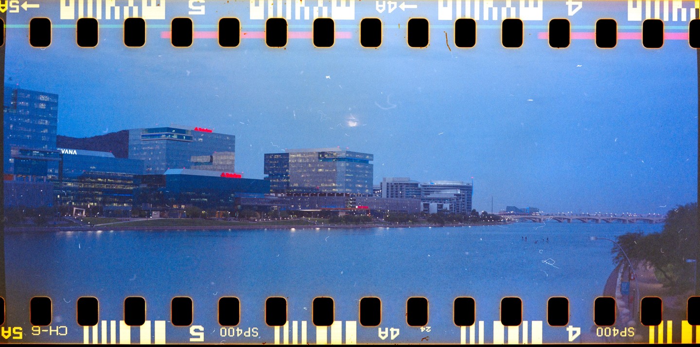 A body of water with buildings and a bridge in the background is visible under a blue sky.