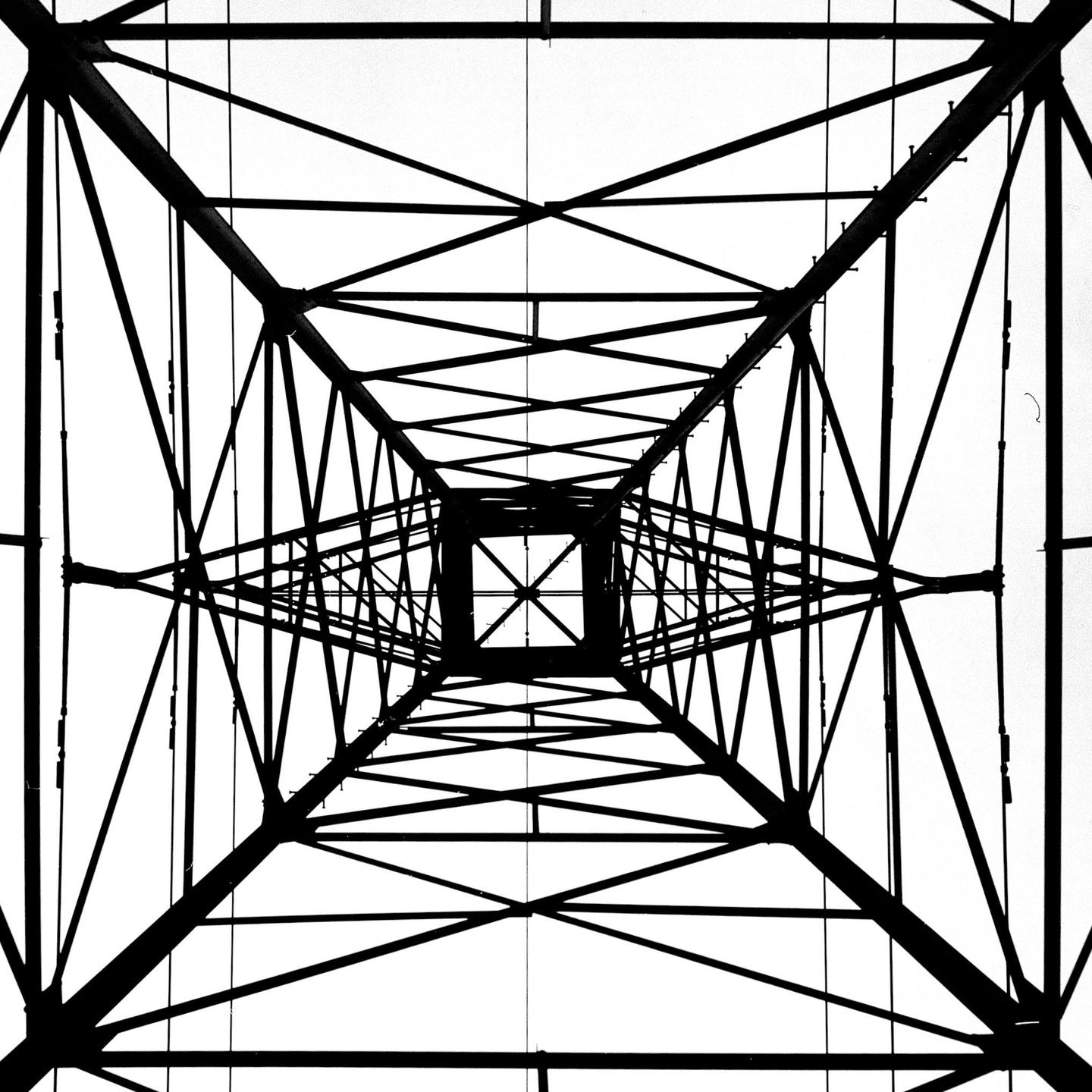 A low-angle, worm's-eye view of a transmission tower shows its intricate metal structure against a white sky.