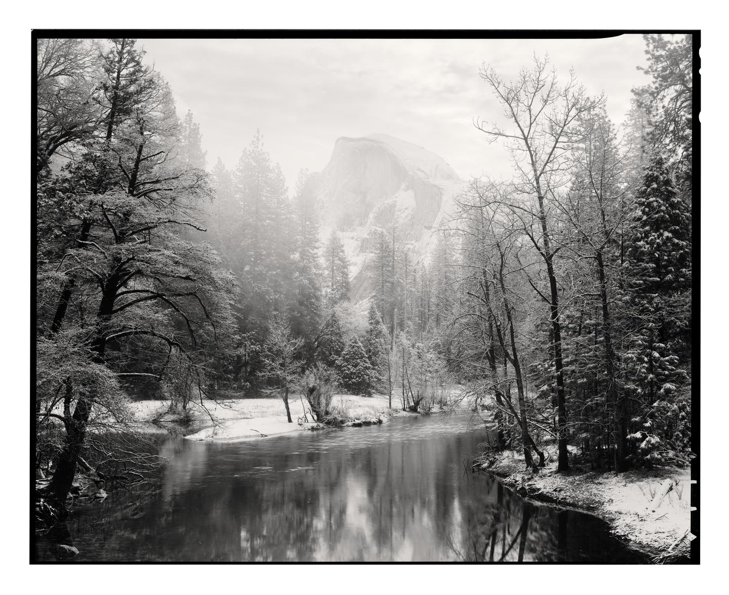 A river flows through a snow-covered forest with a large mountain in the background.