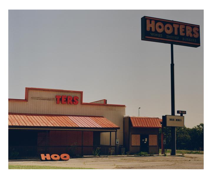 An abandoned Hooters restaurant with a large sign stands under a clear sky.