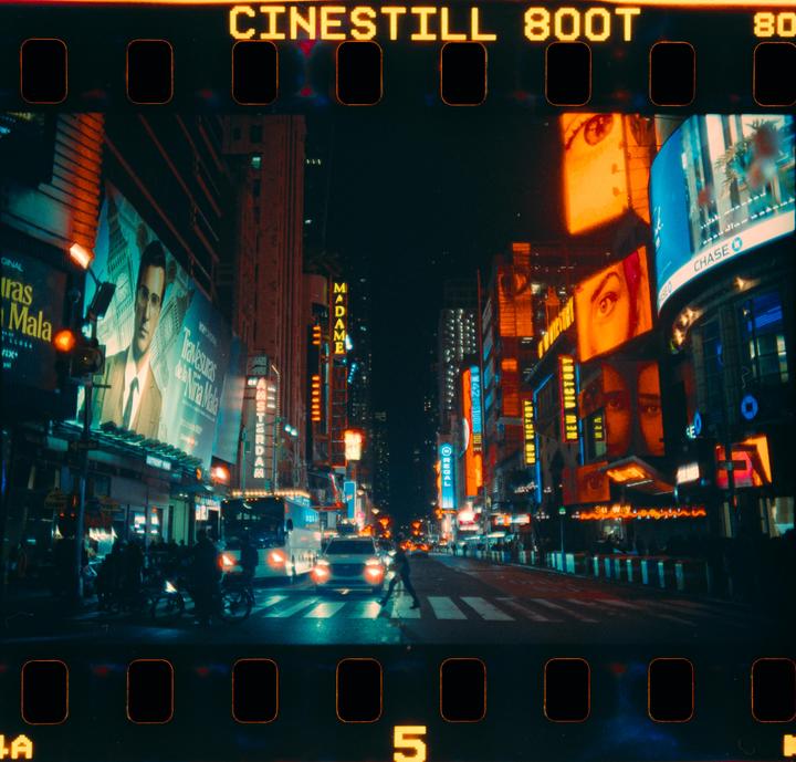 A street at night is illuminated by the neon signs of many buildings and billboards.