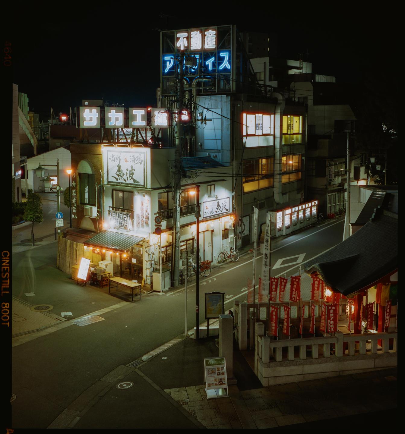 A street in Tokyo is illuminated by neon signs and streetlights at night.
