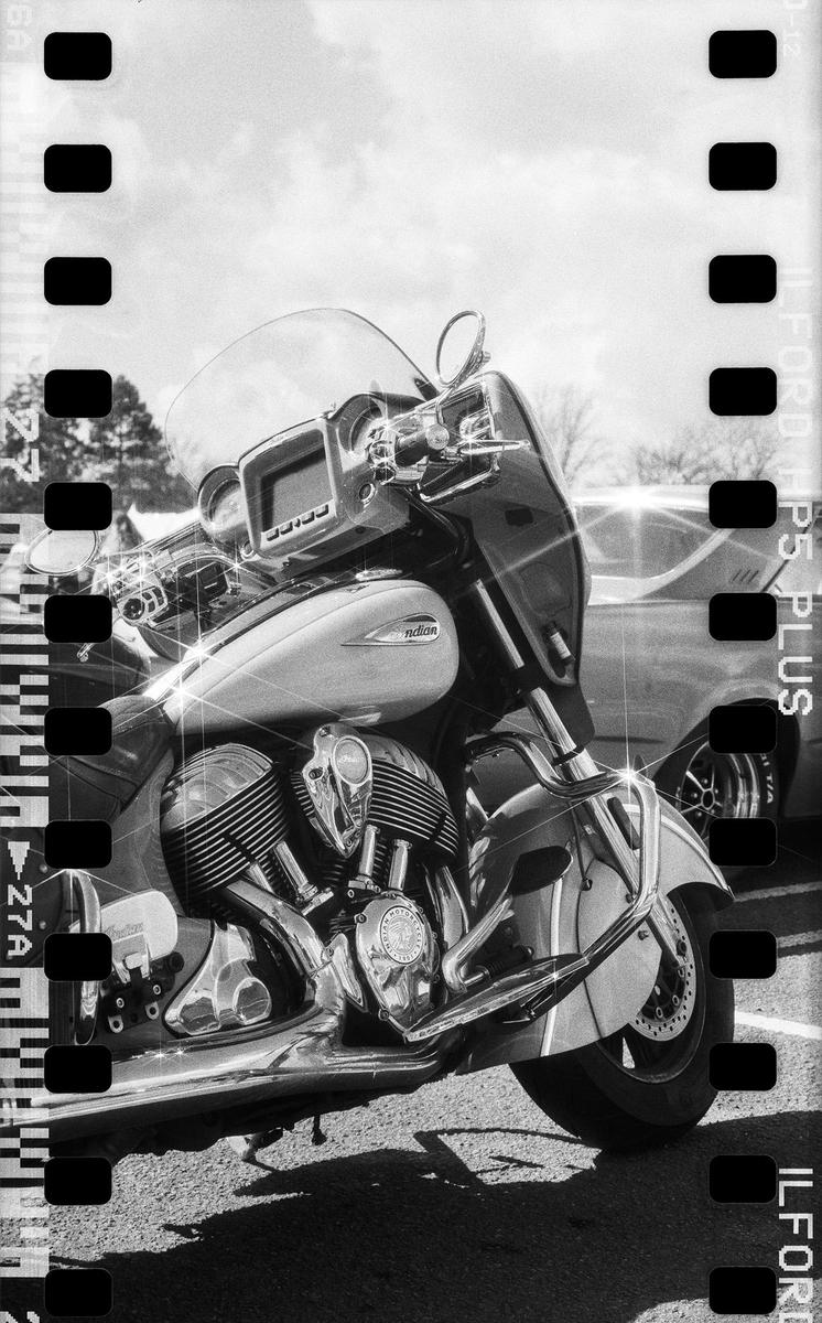 A motorcycle with a large engine and windshield is parked on asphalt with a car in the background.